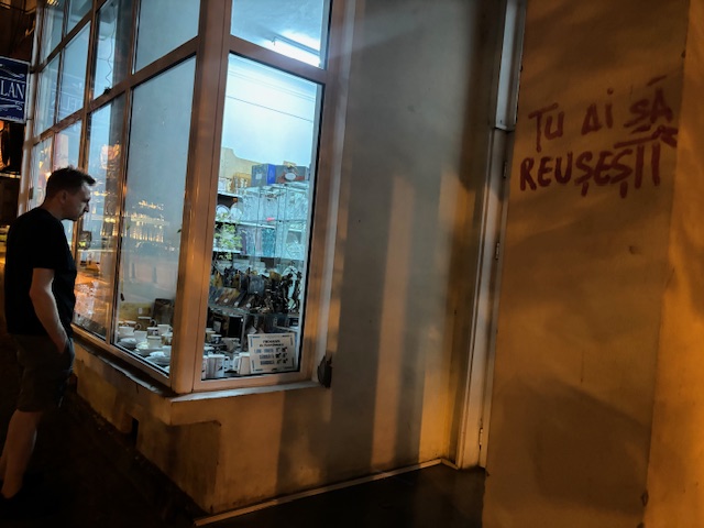 My brother contemplating the window of a store next to a wall covered in graffiti that says "You will succeed," in Iași, Romania